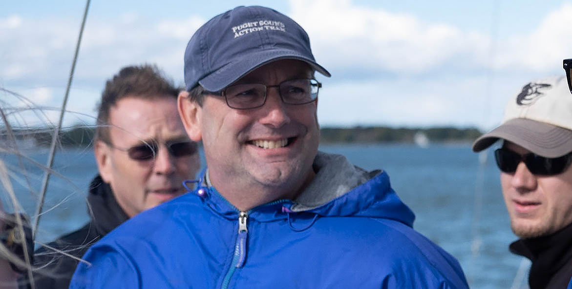 A man in a blue jacket smiling on a boat.