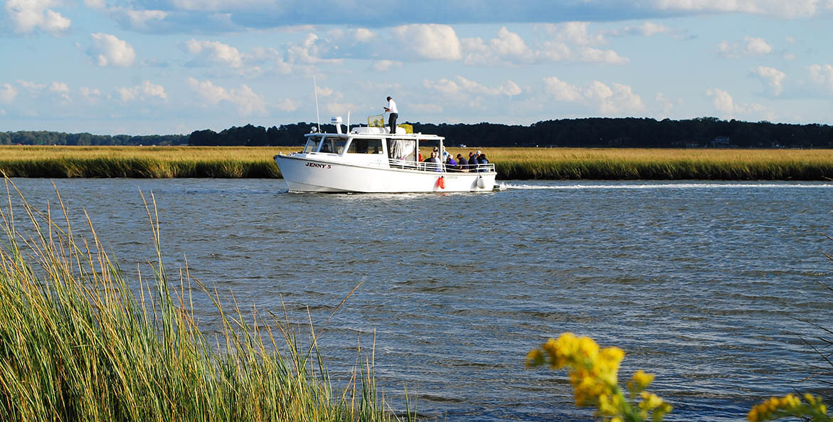 A white work boat on the water with marsh grasses around.