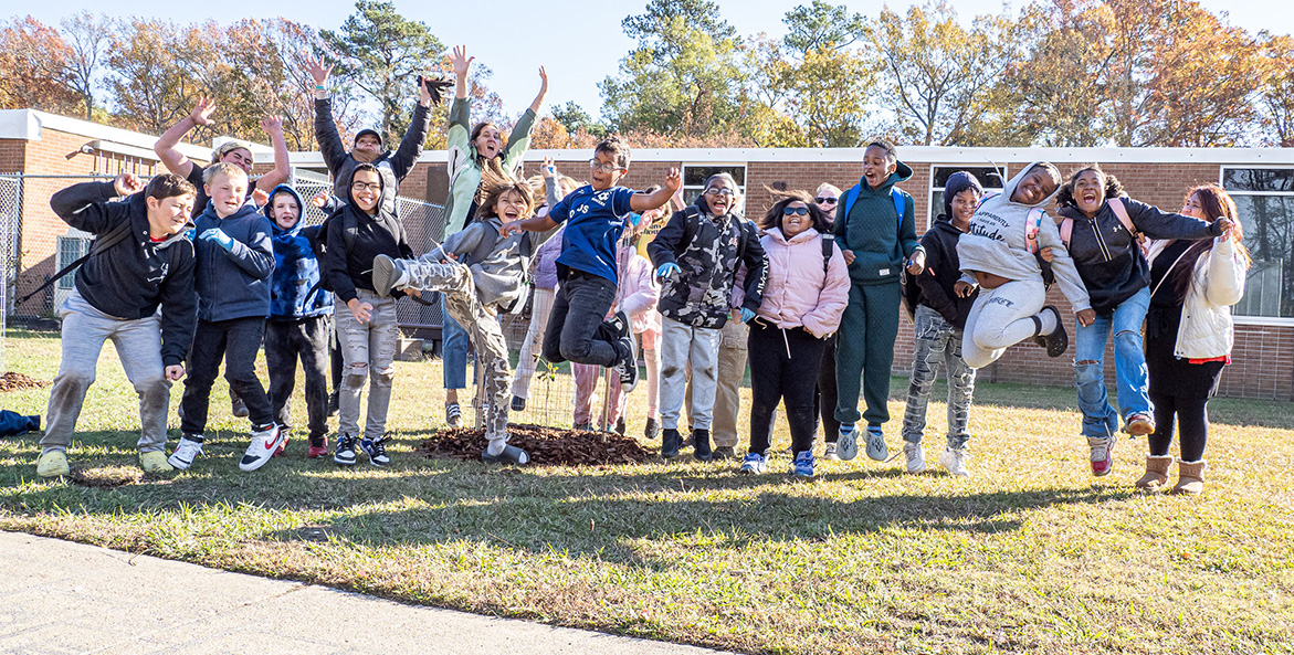 A group of students jump for joy outside their school.