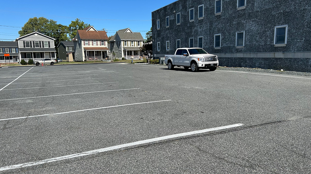 A gray parking lot sits next to a gray cement building.