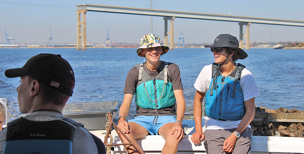 Two students sit on a boat with Baltimore's Key Bridge in the background.