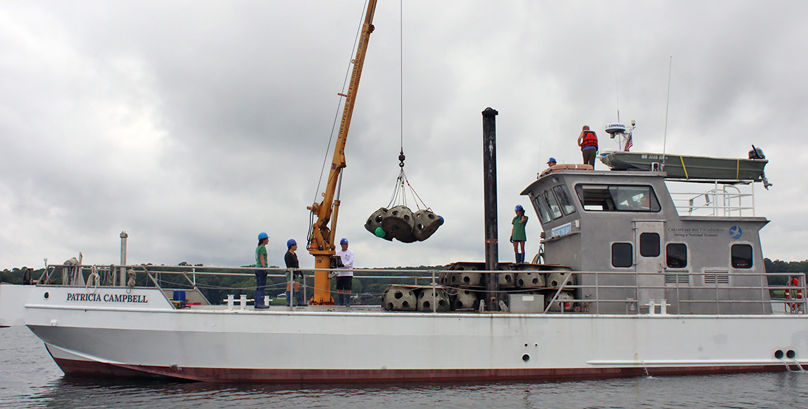 A crane picks four reef balls off the deck of the Patricia Campbell and prepares to lower them into the water.