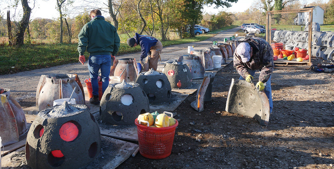 Three men remove concrete reef balls from the forms used to create them.