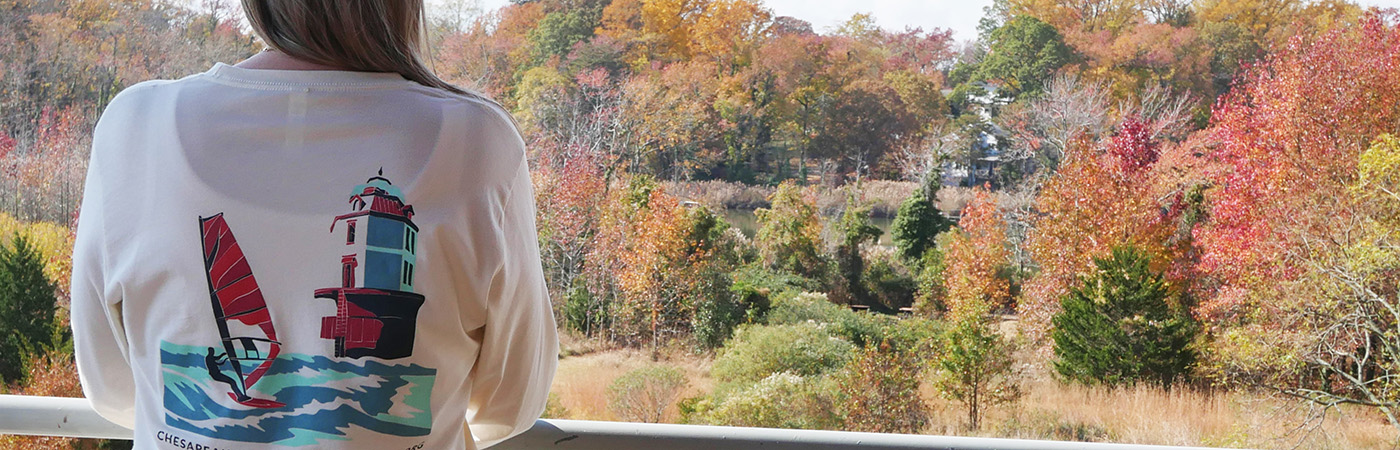 A woman wears a long sleeve t-shirt with back graphics showing a sailboat and lighthouse.